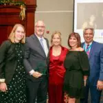 Group of CCR Executives smile for the camera gathered around a glass award in a hotel ballroom setting
