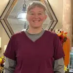 Woman with short hair and red scrubs smiles in front of an octagonal mirror