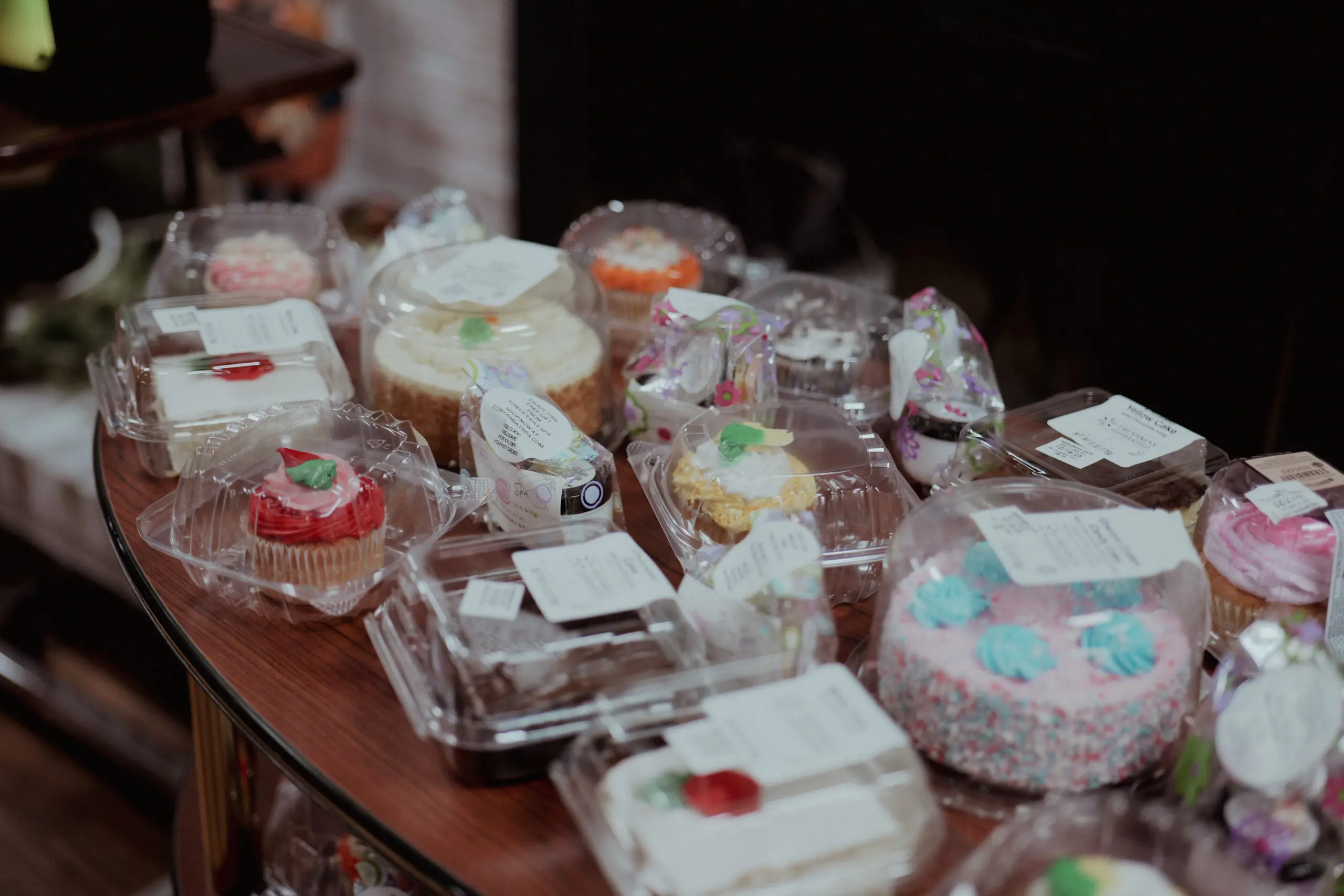 Assortment of frosted cakes and cupcakes in plastic containers on a wooden table