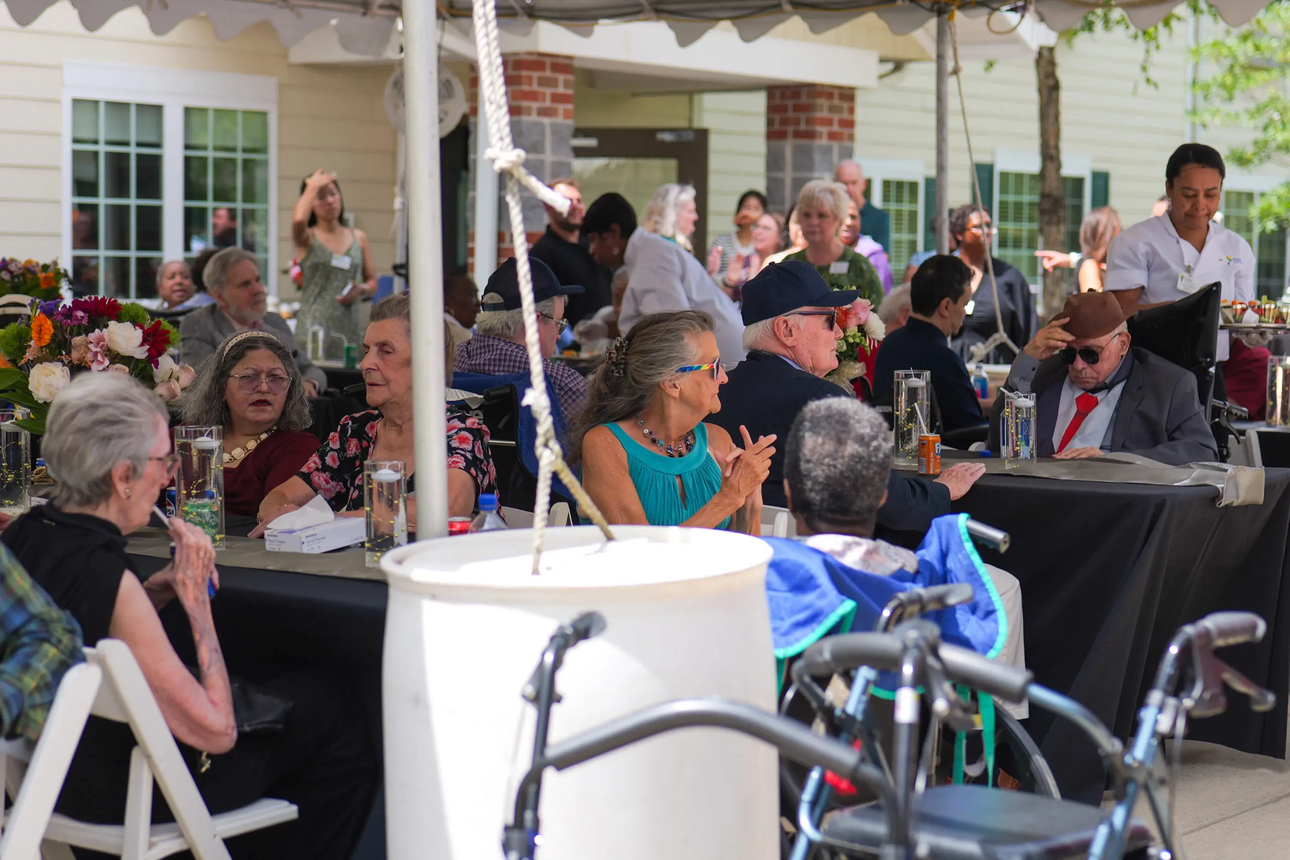 Tables of elderly men and women sitting outdoors under a tent at an event
