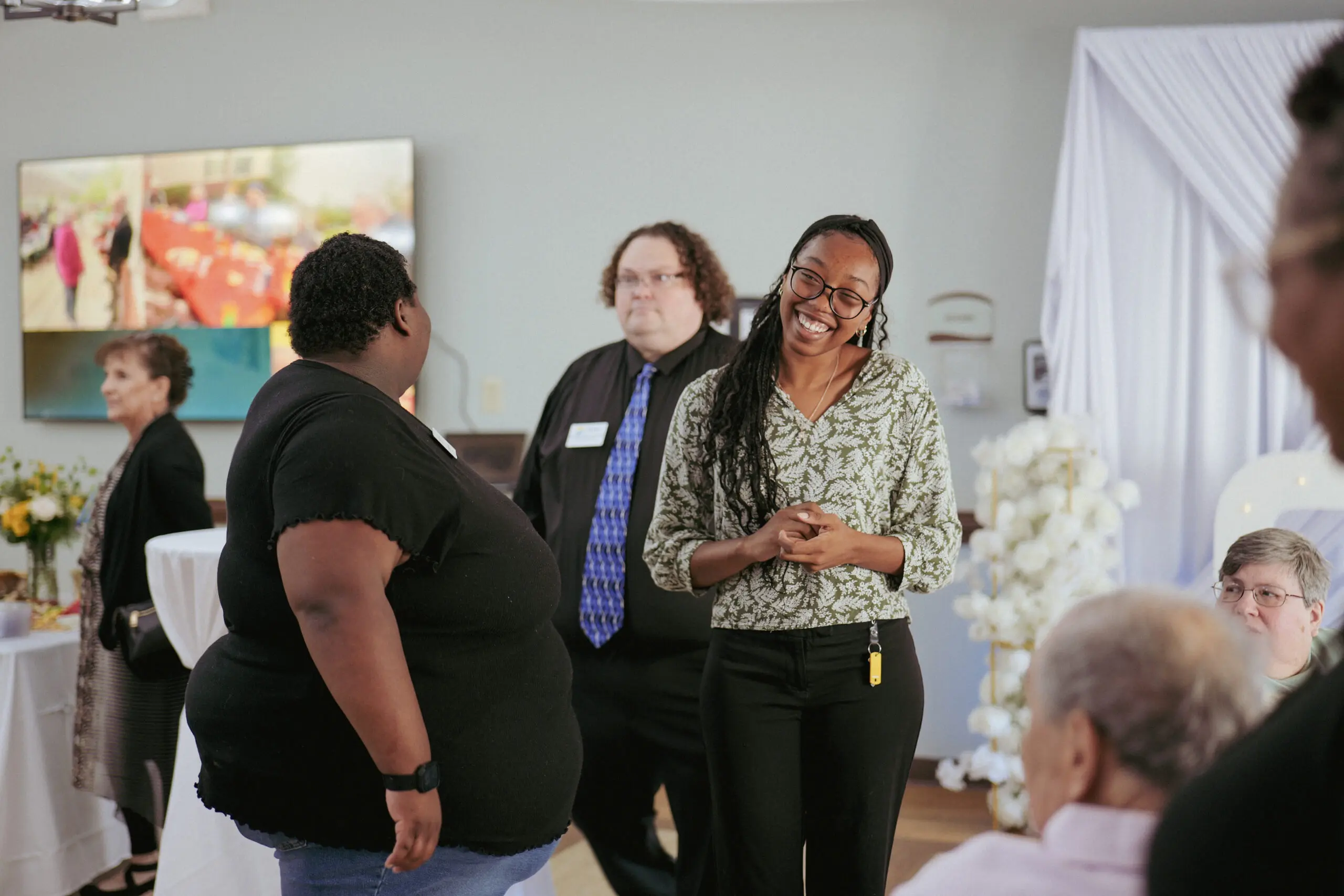 Young woman with long braided hair, glasses, and business clothes laughs with another woman during an event