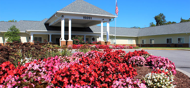 Shot of a luscious bed of pink, red, and white flowers in the foreground with a white and brick building in the background