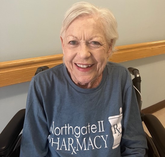 Older woman in a wheelchair and a blue long sleeved tshirt smiles at the camera