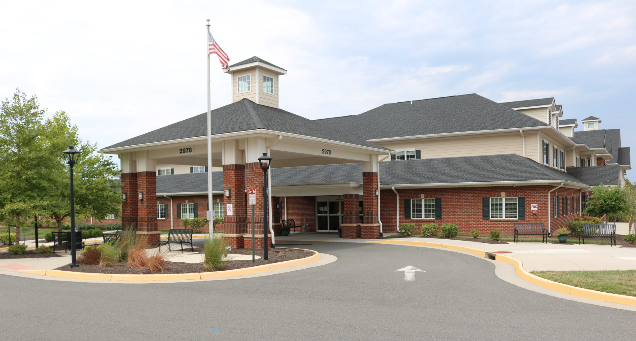 Exterior shot of a tan and brick building and an asphalt driveway beneath a flagpole bearing the American flag