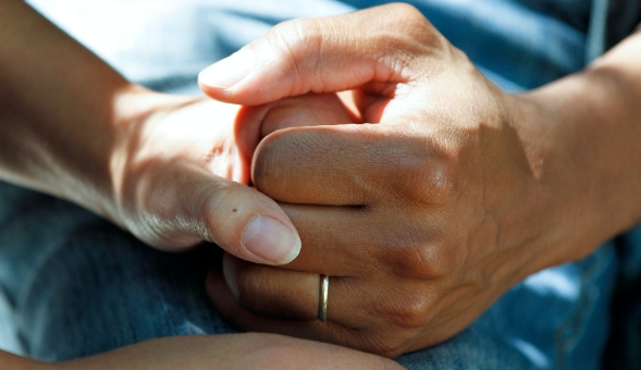 Closeup of holding hands, one of which has a wedding ring on
