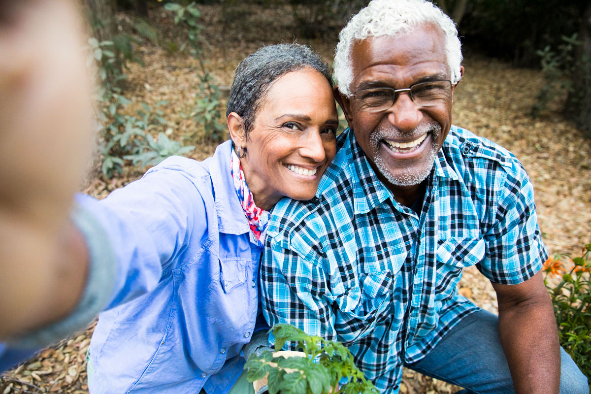 Older man and woman take a selfie while standing in a leaf-strewn yard