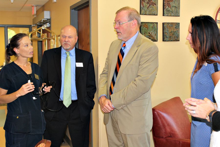 Group of men and women in business clothes stand in a hallway beside a waiting area and talk