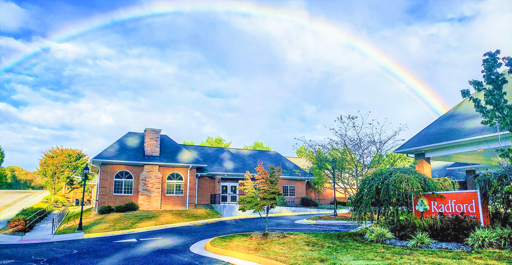 Exterior shot of the Radford Health and Rehab Center building, sign, and parking lot with an arching rainbow overhead