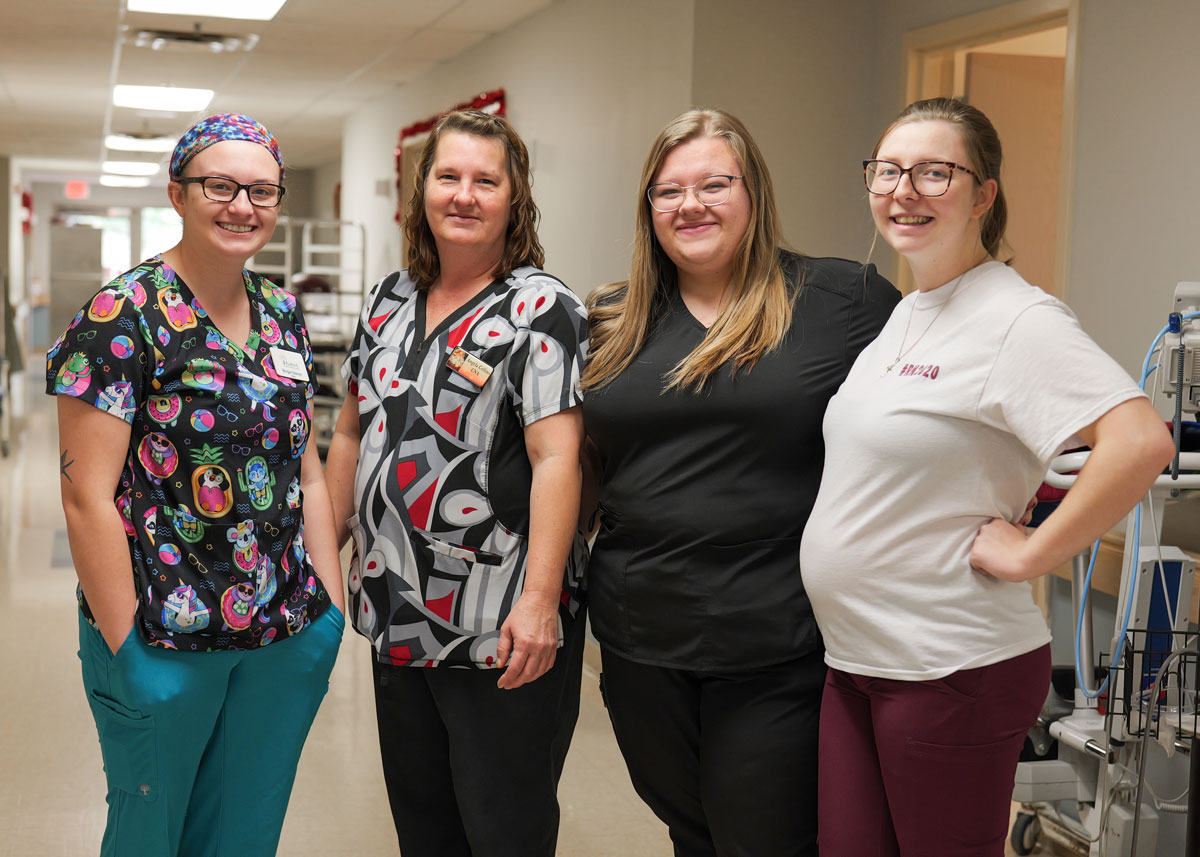 Four female staffers stand in a hallway and smile for the camera together