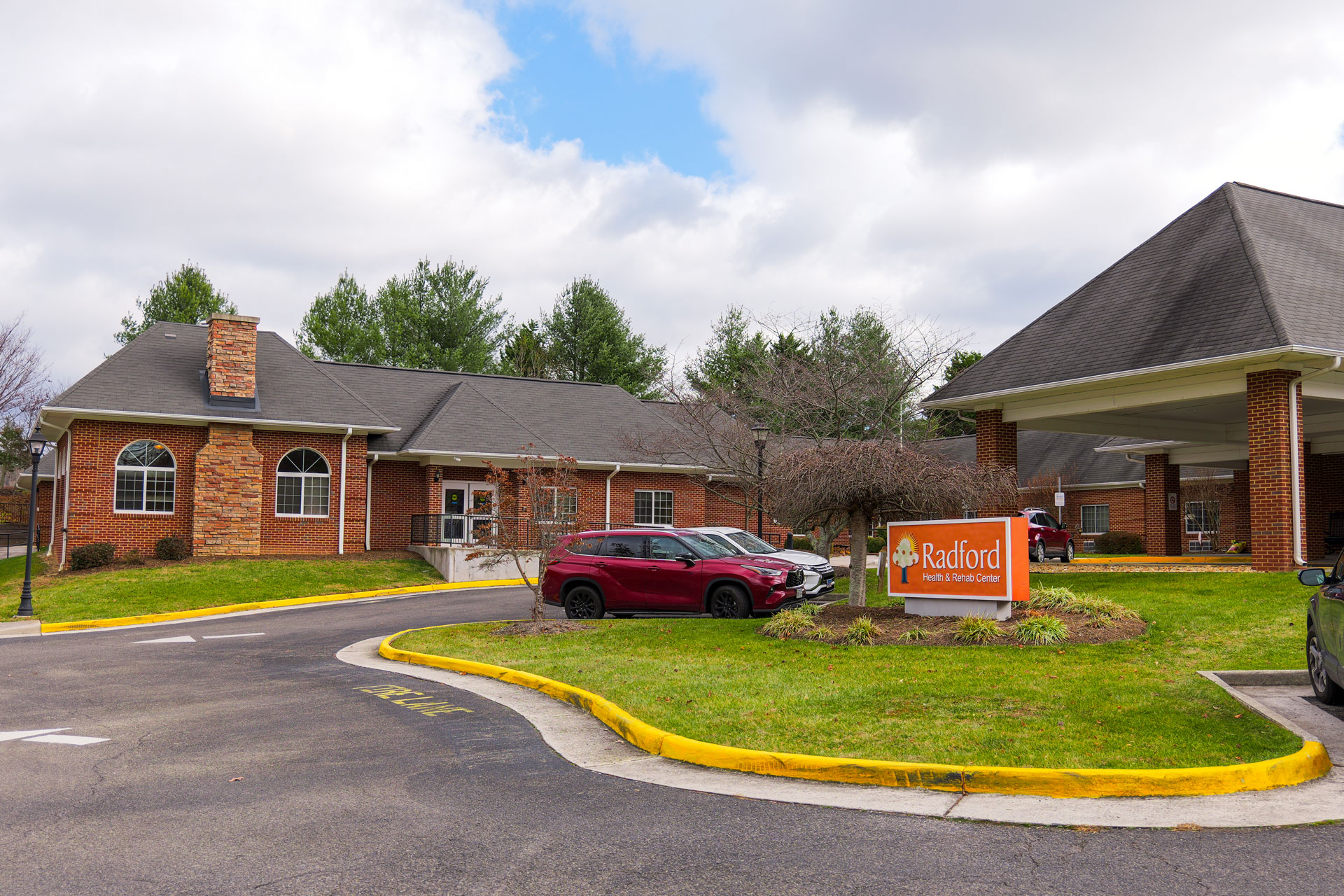 Exterior view of brick building and parking lot, with an orange Radford Health & Rehab Center sign out front