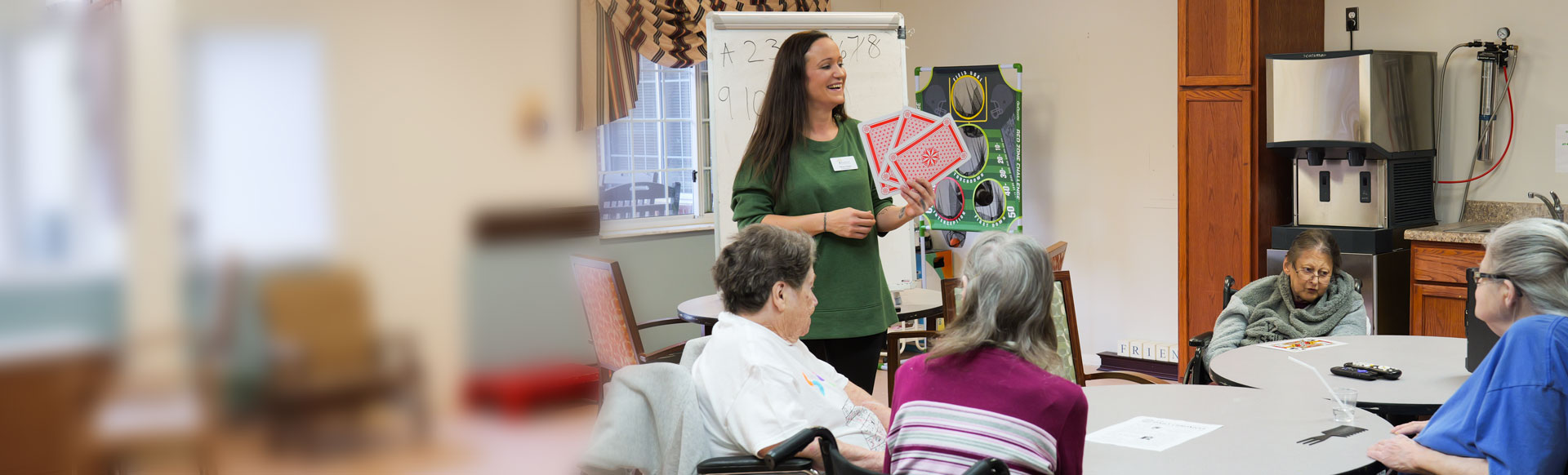 female staff member in a green shirt holds large playing cards and stands in front of a group of seniors