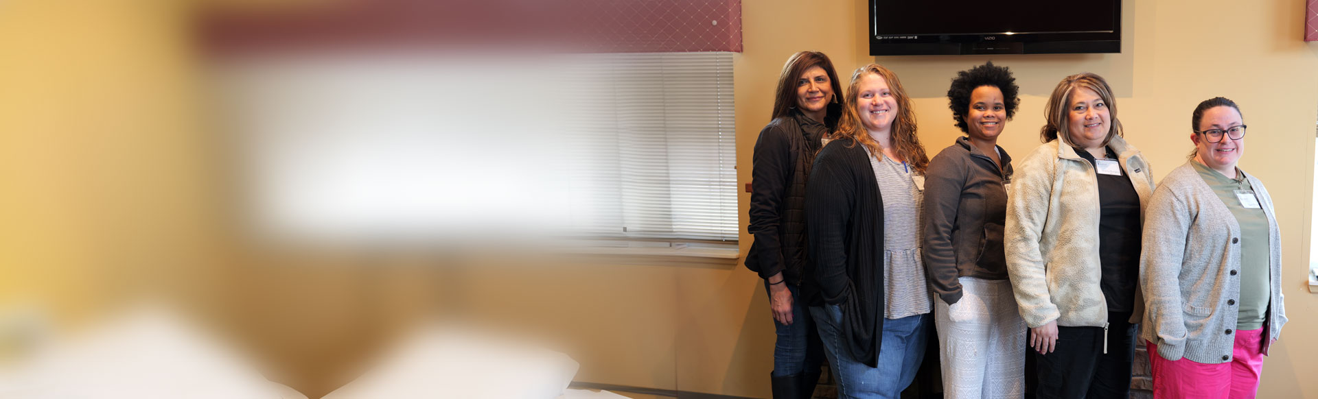 5 female employees standing in a waiting room smiling at camera. The left side of the image is completely blurred
