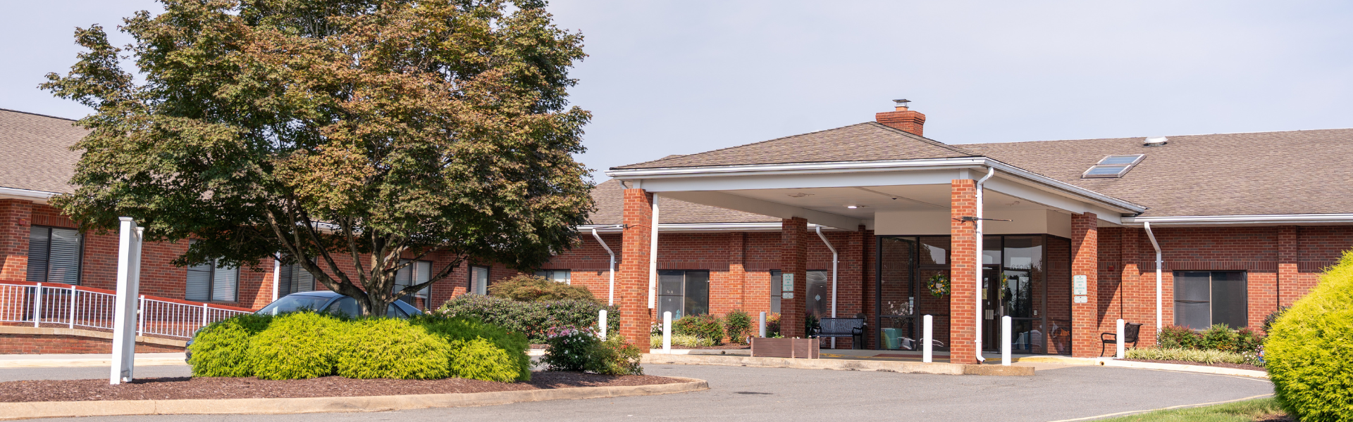 Exterior shot of the Carriage Hill Health & Rehab Center, a one-story brick building with an asphalt loop pull-up parking area
